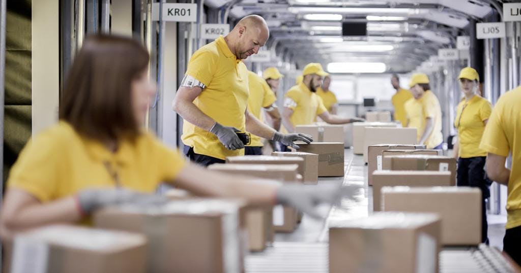 Workers processing boxes on conveyor belt in distribution warehouse.