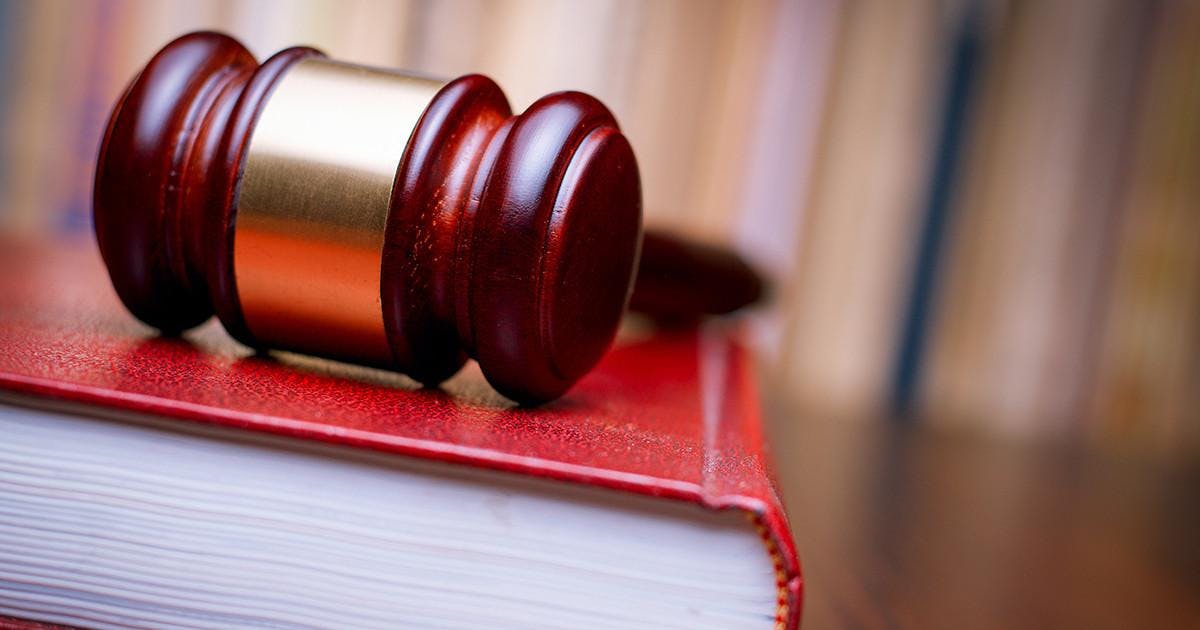 Judges wooden gavel resting on a large red law book on a table in court in a conceptual image of justice and law enforcement