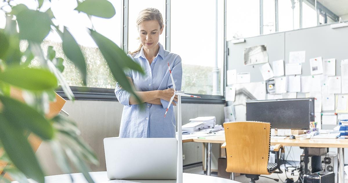 Woman in office with plan, laptop and wind turbine model on table